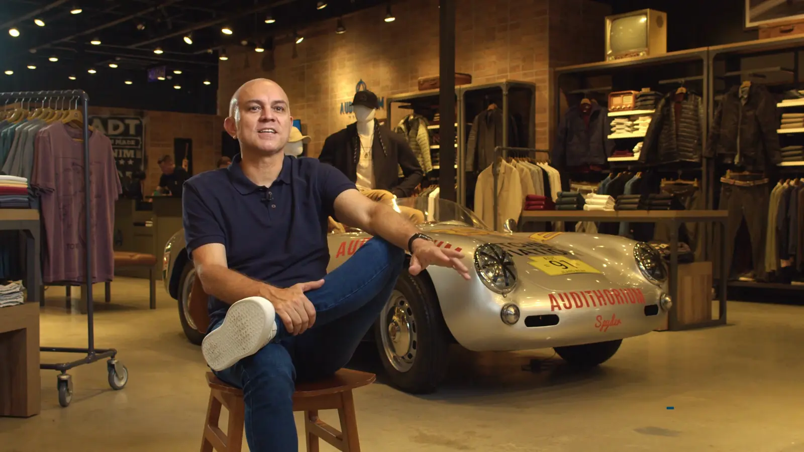 Alexandre, fundador da Audithorium, sentado ao lado de um carro esportivo antigo dentro de uma das lojas